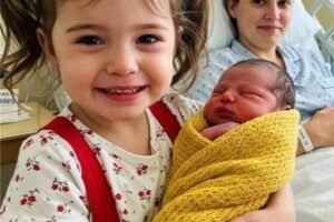 MY DAUGHTER WAS THRILLED TO HOLD HER NEWBORN SISTER—UNTIL SHE WHISPERED ONE WORD THAT SHOOK ME TO MY CORE ==== She sat cross-legged at the edge of the hospital bed, her little hands trembling as they gently cradled the bundle in her lap. My oldest, Lina—just four years old, dressed in her favorite red suspenders and crooked ponytail—looked like she was holding the universe. Her eyes sparkled with something beyond excitement. Reverence, maybe. Or… something I couldn’t place. The room smelled of antiseptic and warm skin. My body ached from the birth, stitches pulling with every breath, but all I could feel in that moment was gratitude. I had worried endlessly during the pregnancy—how would Lina adjust? Would she feel forgotten? But there she was, beaming. Whispering soft “shh” sounds. Rocking just slightly. Everything seemed perfect. Then, she leaned forward. Her face nearly touching her newborn sister’s. And she whispered, “Now I have someone.” I smiled through tears. “Someone to what, baby?” She didn’t look up. Still watching the baby, still swaying. “To keep the secrets with,” she whispered. I felt a chill crawl up my spine. “Secrets?” I asked, trying to sound calm. She finally looked up at me then—eyes wide, too knowing, too old. She nodded slowly, her voice clear now. “Like the ones I don’t tell Daddy.” And before I could speak, before I could push the panic down or reach for her tiny hand, she leaned in again and whispered something else. Something that made the heart monitor skip a beat. Something that made the nurse in the doorway freeze. She said— (Continued in the first —what Lina revealed next changed everything I believed about our home…)
